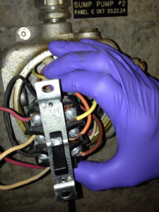 An electrician's gloved hand wiring a sump pump electrical component for Boweaks Electrical Solution LLC in Honolulu, HI.