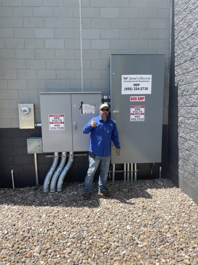 An electrician from Jesse's Electric giving a thumbs up next to a newly installed electrical panel in Laredo, TX.