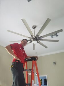 An electrician from Small Jobs Electric in Tampa, FL, standing on a ladder next to a large ceiling fan he has installed.