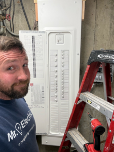 An electrician proudly standing next to a newly installed electrical panel for Mr. Electric of Rogers in Rogers, AR.