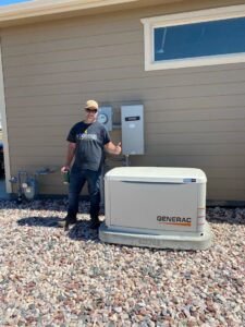 An electrician from J&S Power Systems and Small Engine giving a thumbs up next to a newly installed Generac standby generator and electrical panel in Laramie, WY.