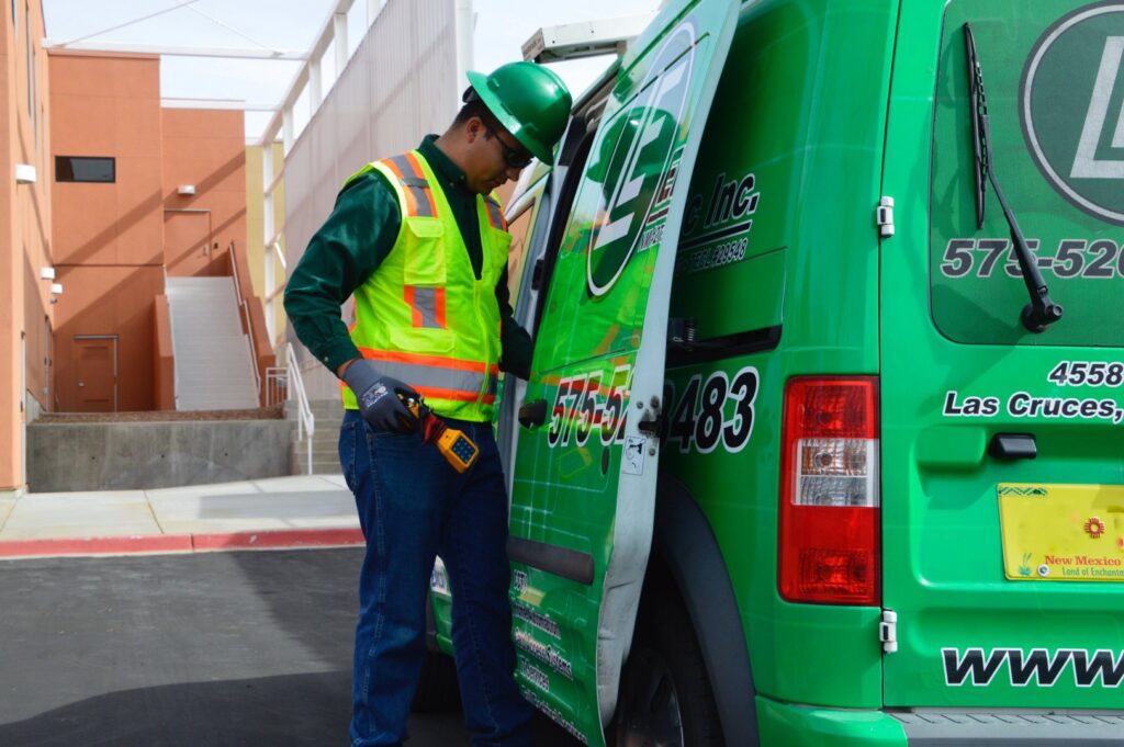 An electrician in safety gear retrieving tools from an LE Electric service van in Las Cruces, NM