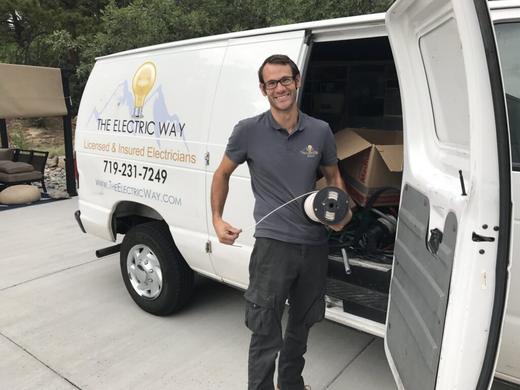 An electrician from The Electric Way in Colorado Springs, CO, standing by their service van with a spool of electrical wire.