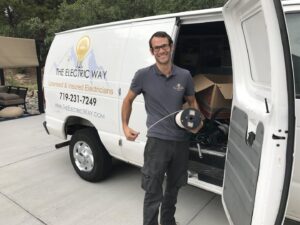 An electrician from The Electric Way in Colorado Springs, CO, standing by their service van with a spool of electrical wire.
