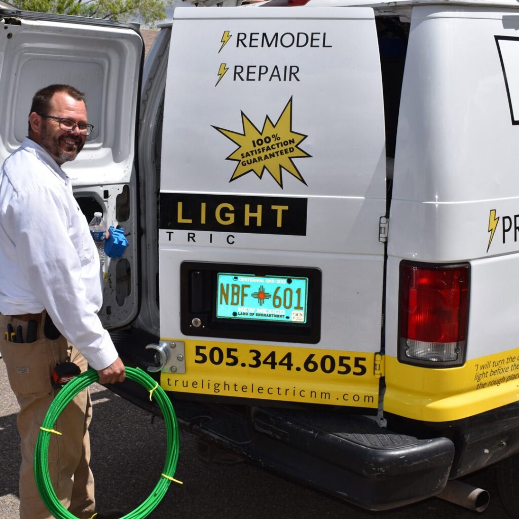 An electrician holding a coil of green wire next to a True Light Electric service van in Albuquerque, NM.