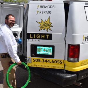 An electrician holding a coil of green wire next to a True Light Electric service van in Albuquerque, NM.