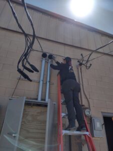 An electrician on a ladder working on exterior electrical conduit and wiring for The Specialist Electrical Contractor in Albuquerque, NM.
