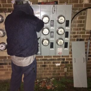 An electrician working on multiple exterior electrical meters and panels at night for Volt Doctors in Durham, NC