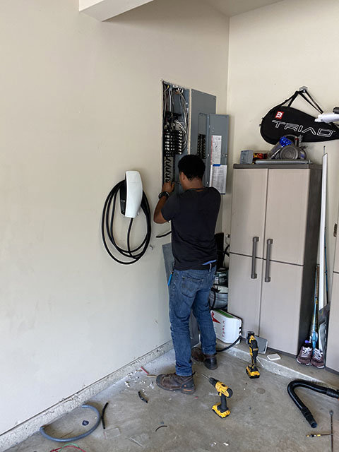 An electrician from High Electrical working on a garage electrical panel, near an EV charger in Atlanta, GA.