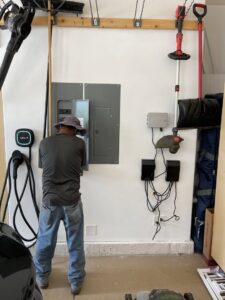 An electrician working on an electrical panel in a garage, with an EV charger visible, for Flowers Electric in Aurora, CO.