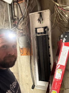 An electrician with a headlamp working on an open electrical breaker panel for Mr. Electric of Rogers in Rogers, AR.