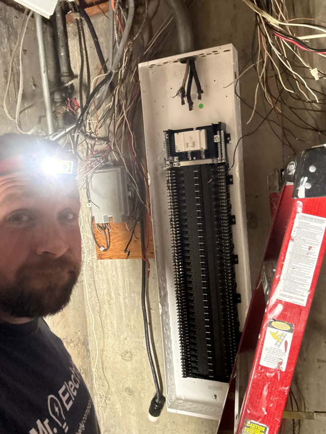 An electrician with a headlamp working on an open electrical breaker panel for Mr. Electric of Rogers in Rogers, AR.