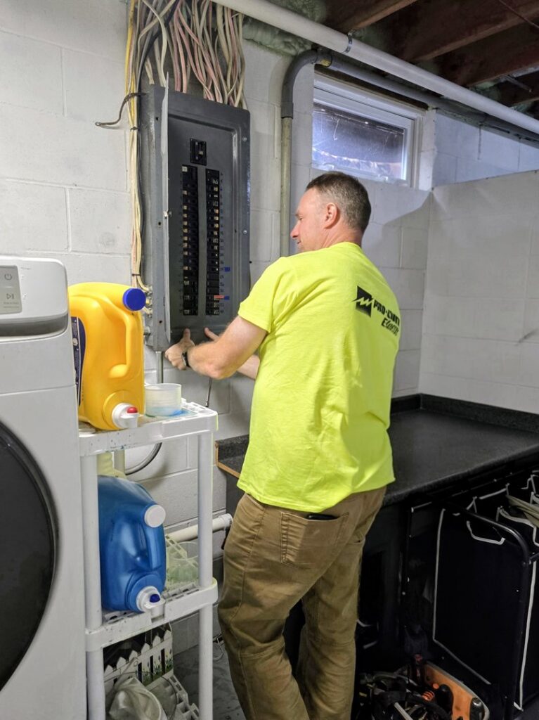 An electrician from Pro Circuit Electric working on an open electrical breaker panel in a residential basement in Peoria, IL.