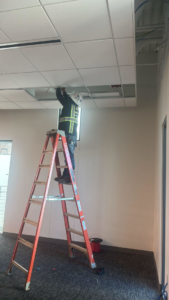 A Reyes Electric Company electrician on a ladder performing ceiling electrical work in Dallas, TX.