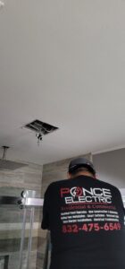 An electrician from Ponce Electric in Houston, TX, working on a ceiling fixture installation in a bathroom