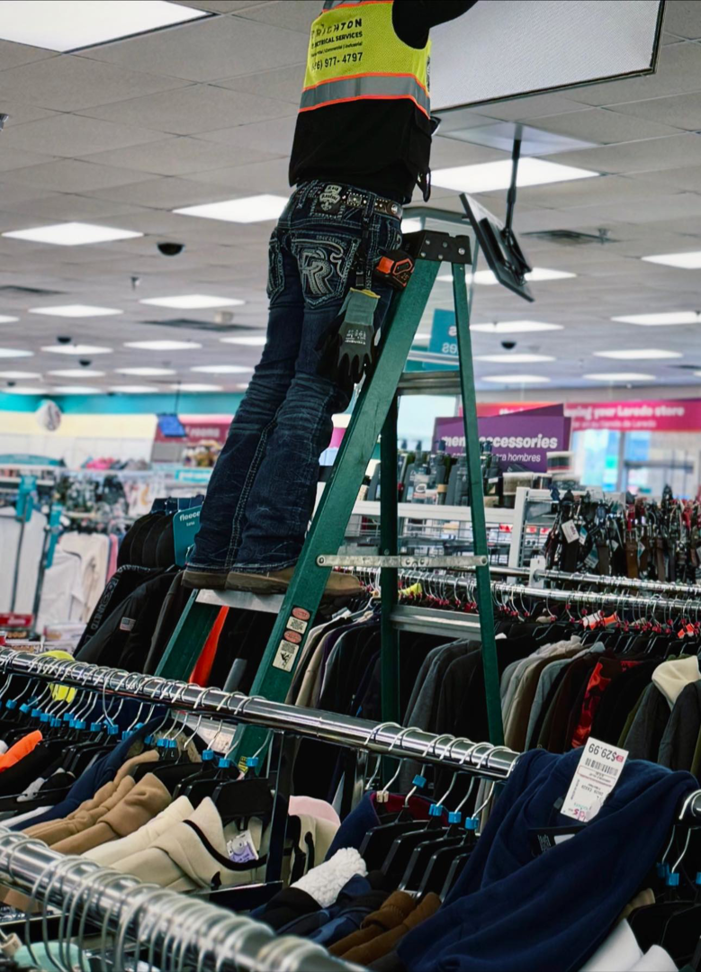 An electrician from Brighton Electrical Services working on a ceiling light fixture in a retail store in Laredo, TX.
