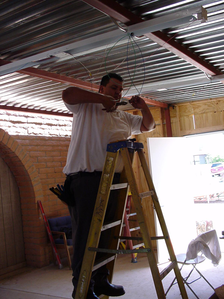 An electrician from Accel Electric on a ladder, working on ceiling wiring and conduit in Peoria, AZ.