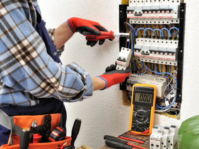 An electrician working on a circuit breaker panel with tools and a multimeter for BrotherlyLove Electric LLC in Houston, TX.
