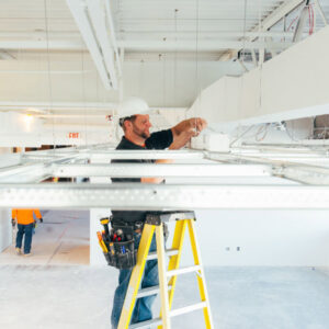 An electrician working on commercial lighting and wiring on a ladder for Brase Electrical Contracting Corp in Omaha, NE.