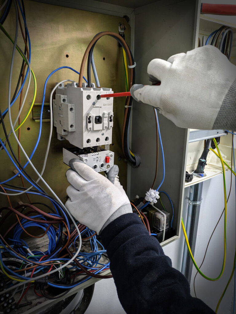 Electrician's gloved hands working on complex wiring inside a panel for Omni Power Electrical Services LLC in San Antonio, TX