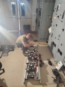 An electrician kneeling and working on an open electrical control panel for Dobson Electric, Inc. in Jacksonville, FL.