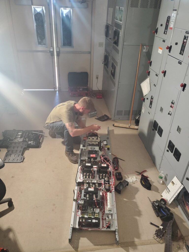 An electrician kneeling and working on an open electrical control panel for Dobson Electric, Inc. in Jacksonville, FL.