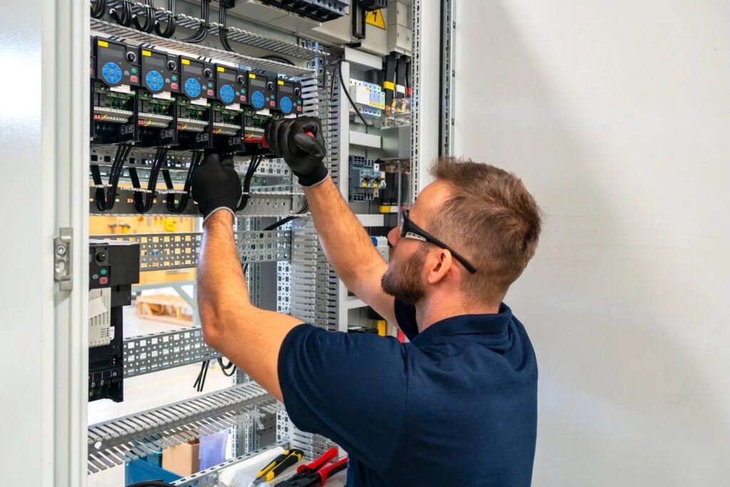 An electrician in safety glasses and gloves working on a complex electrical control panel for Next Level Contracting LLC in Dayton, OH