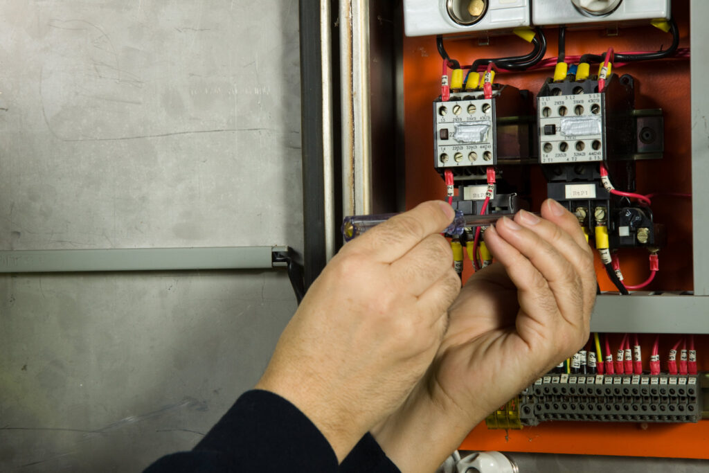 An electrician's hands working on complex wiring inside an open electrical control panel for TJS Electrical Services Inc in Mesa, AZ.