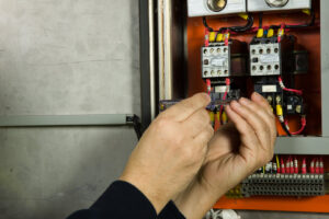 An electrician's hands working on complex wiring inside an open electrical control panel for TJS Electrical Services Inc in Mesa, AZ.
