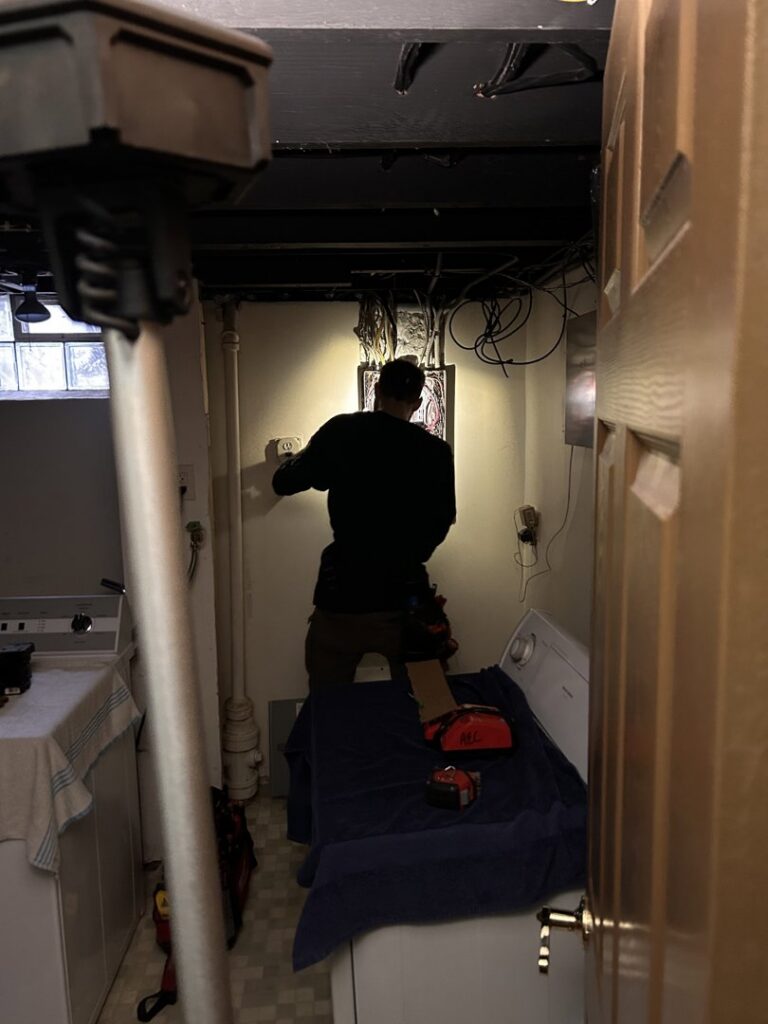 An electrician working on an electrical box in a laundry room for Advance Electrical Contractors in Milwaukee, WI.