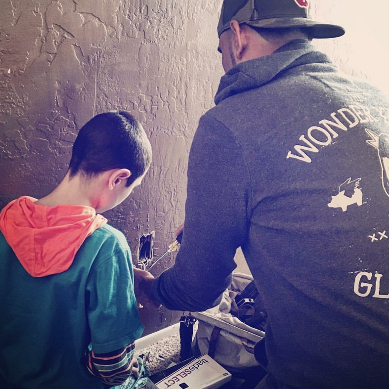 An electrician from Reuben Electrical Contracting working on an electrical box with a child observing in Scottsdale, AZ.