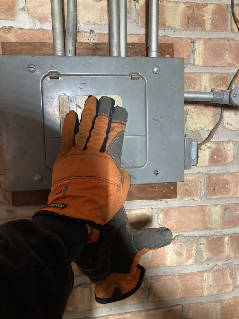A gloved hand of an electrician from Diaz Techician LLC in Chicago, IL, working on an electrical junction box with conduit.