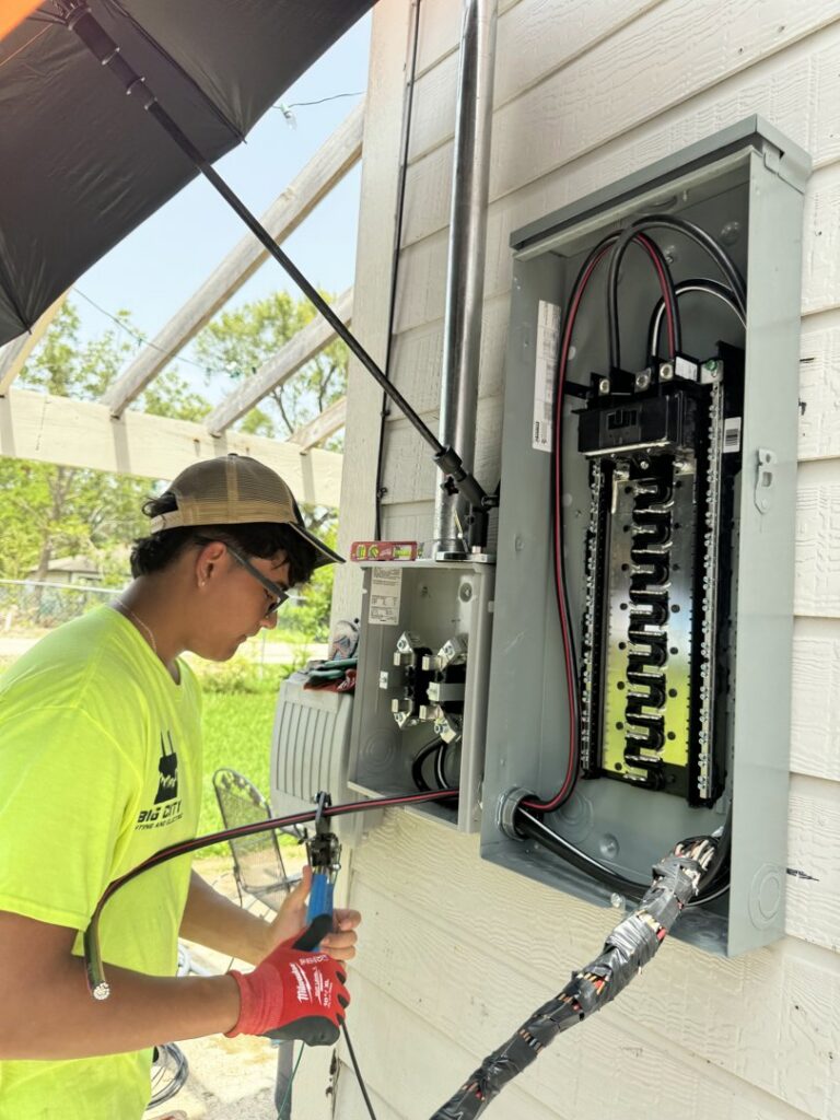 An electrician from Big City Lighting and Electric working on an outdoor electrical panel, cutting wires with pliers in Houston, TX.