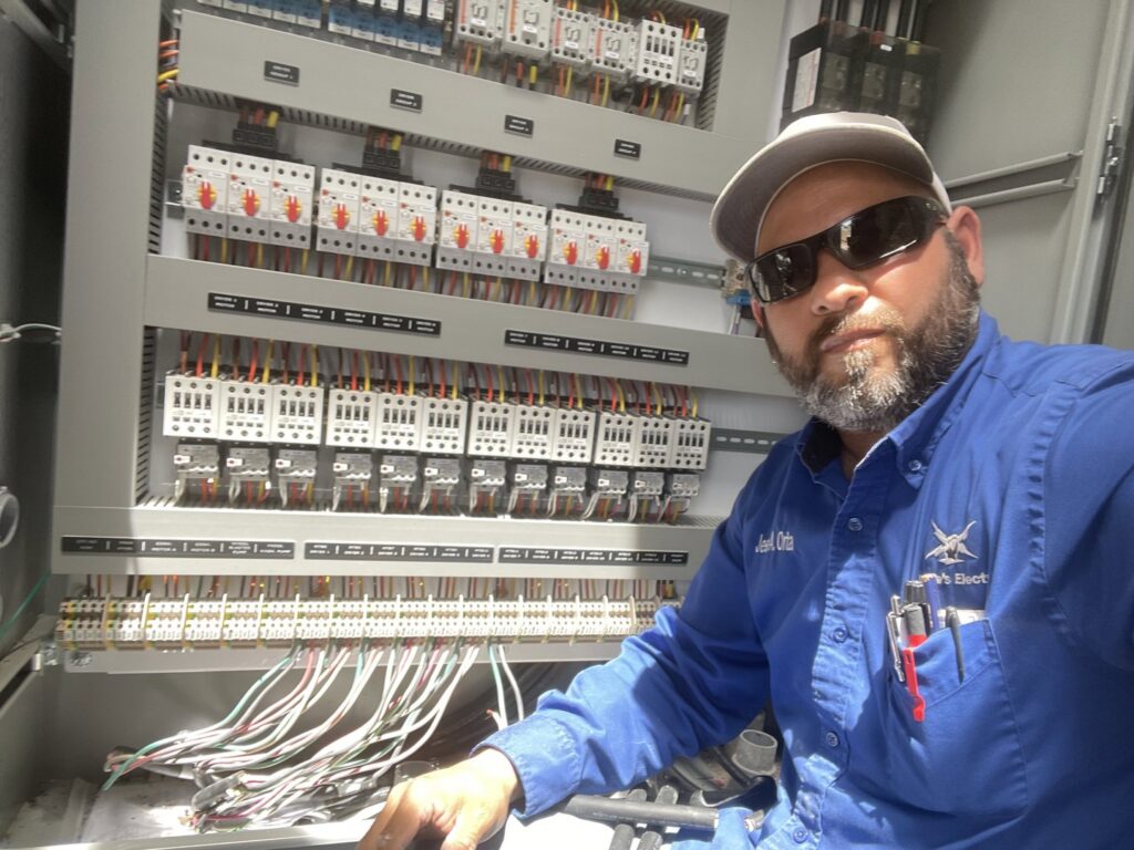 An electrician from Jesse's Electric working on an open electrical panel with numerous wires and circuit breakers in Laredo, TX.