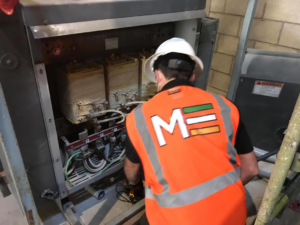 An electrician in a hard hat working on an electrical panel for Mulholland Electric Inc in San Francisco, CA.