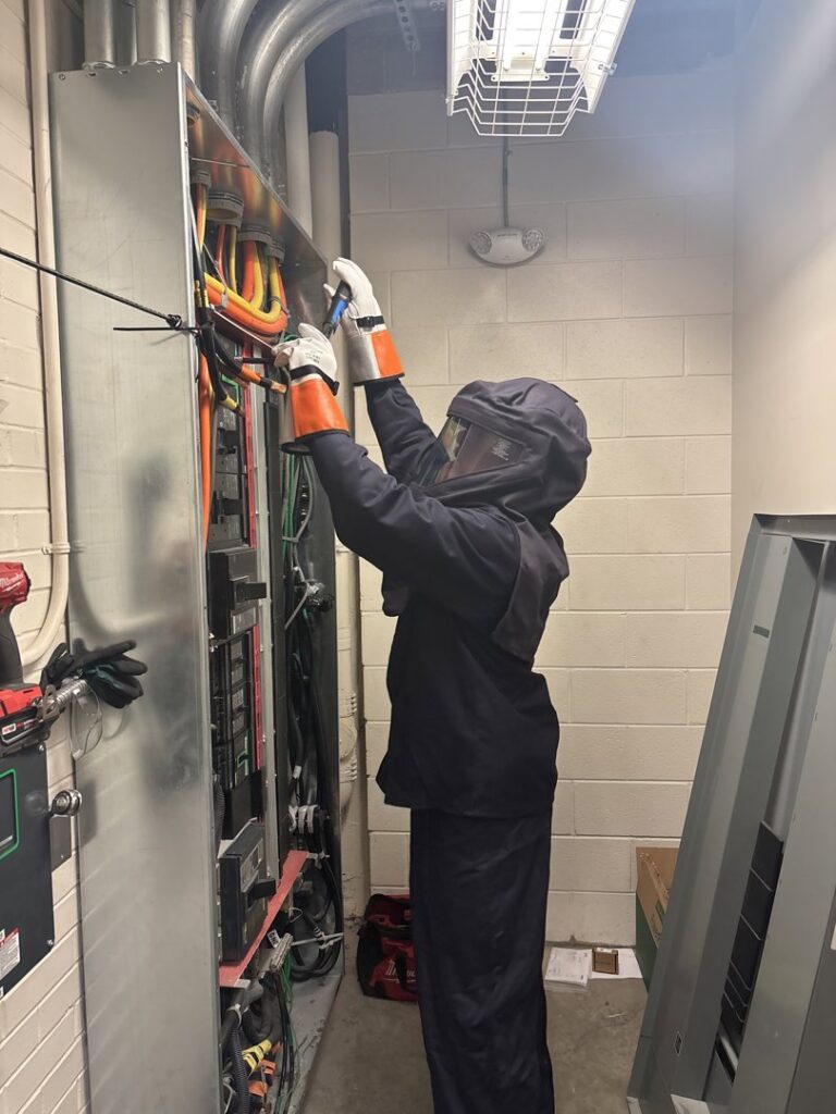 An electrician in arc flash PPE working on an electrical panel for Onsite Electrical Services in Raleigh, NC.