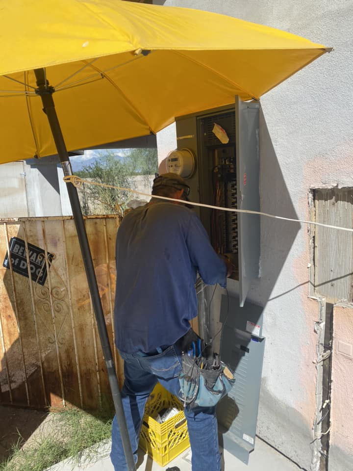 An electrician working on an outdoor electrical panel under an umbrella for Sahuaro Electric LLC in Tucson, AZ.
