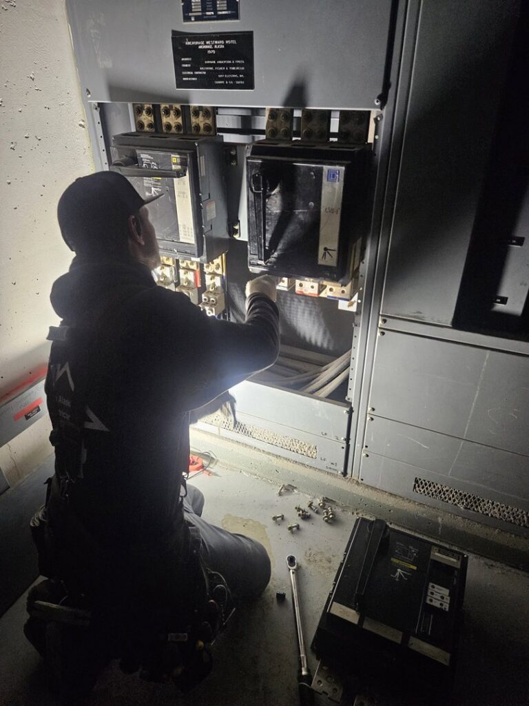 An electrician from The Alaskan Electricians working on an electrical panel in Anchorage, AK, illuminated by a headlamp.