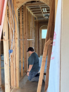 An electrician kneeling to work on electrical rough-in wiring and blue boxes in a new home by ASTS Electric in West Monroe, LA.