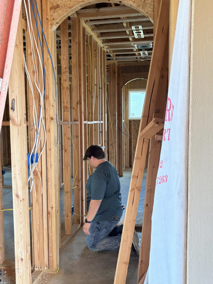 An electrician kneeling to work on electrical rough-in wiring and blue boxes in a new home by ASTS Electric in West Monroe, LA.