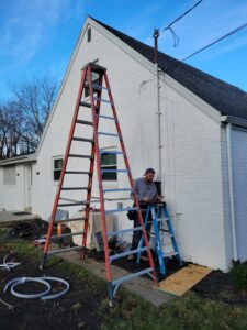 An electrician from Maiolo Electric working on the exterior electrical service of a residential building in Pittsburgh, PA, using a ladder.