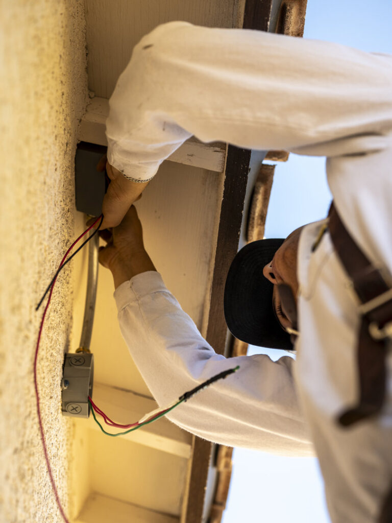 An Electricode electrician working on exterior electrical wiring under the eaves of a building in Las Vegas, NV.