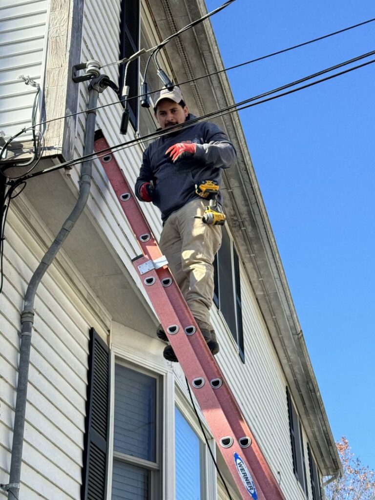 An electrician on a ladder performing exterior wiring work for Ramos Electrical services inc in Brownsville, TX
