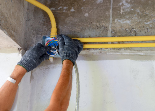 An electrician's hands working on wiring inside an electrical junction box with conduits for BrotherlyLove Electric LLC in Houston, TX.