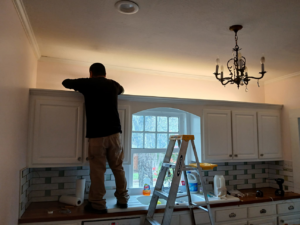 An electrician from Jesano Electric in Fort Worth, TX, working on electrical wiring above kitchen cabinets.