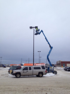 An electrician from Sabteck Electric working on a tall light pole in a snowy parking lot in Timmins, ON