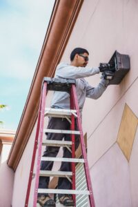 An electrician on a ladder working on an outdoor electrical box or fixture for Electrical Power Source in Fresno, CA.