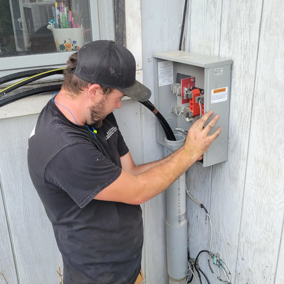 An electrician from Alpha Electric LLC working on an outdoor electrical panel and meter box in Dover, NH.