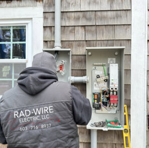 An electrician from RAD-WIRE ELECTRIC, LLC working on an outdoor electrical panel and transfer switch in Manchester, NH.