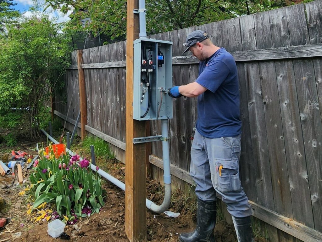 An electrician working on an outdoor electrical service panel mounted on a wooden post for Beaver Electric in Hillsboro, OR.